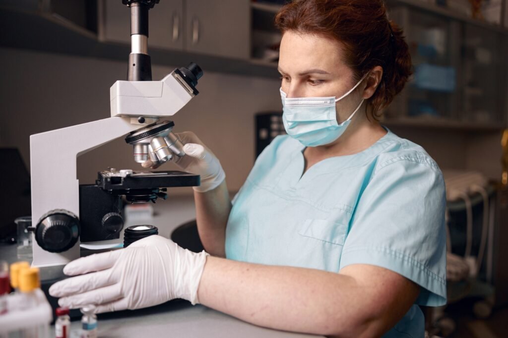 Woman lab assistant works with microscope to research material sample in clinic